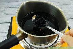 a person holding a spoon over a pot filled with black liquid on top of a stove