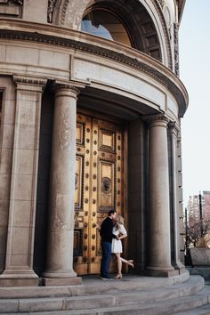 a man and woman are standing in front of a large gold door with columns on each side