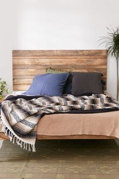 a bed with pillows and blankets on it next to a potted plant in the corner