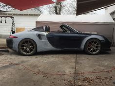 a blue and gray sports car parked in front of a garage with an awning