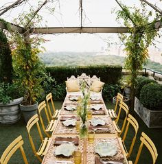 an outdoor dining table set with yellow chairs and place settings for dinner on the grass