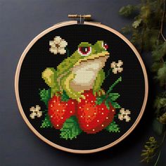 a cross stitch frog sitting on top of strawberries