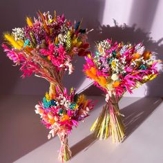 two vases filled with colorful flowers sitting on top of a white table next to each other