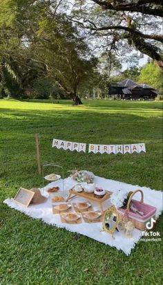 an outdoor picnic with food and drinks on the grass in front of a sign that says happy birthday