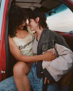 two young women sitting in the back of a red truck, one holding her arm around the other's shoulder