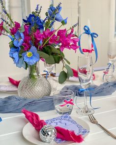 the table is set with blue and pink flowers in vases, napkins, and silverware