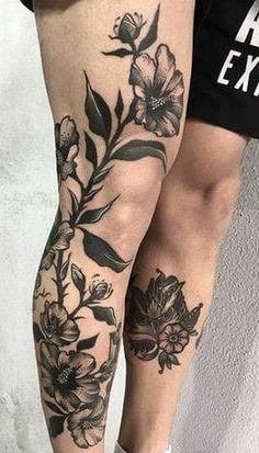 a woman's legs with flowers and leaves tattooed on her leg, while standing next to a wall