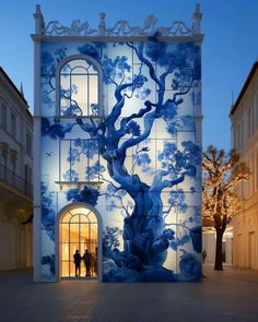 two people standing in front of a blue and white building with trees painted on it