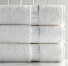 four white towels stacked on top of each other in front of a tiled bathroom wall