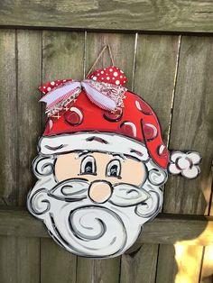 a santa clause hanging on the side of a wooden fence with a red hat and beard