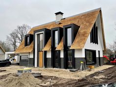 a house that is being built with wood shingles on the roof and two cars parked in front of it