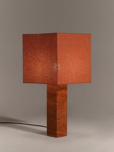 a wooden table lamp with a red shade on the top and an electric cord plugged into it