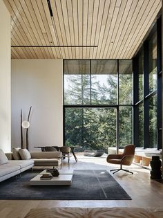 a modern living room with large windows and wood ceilinging, along with an area rug on the floor