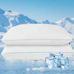 two pillows with ice cubes in the water next to each other and mountains behind them