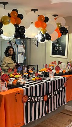 a woman standing in front of a table filled with food and balloons hanging from the ceiling