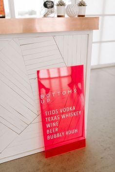 a red sign sitting on top of a counter next to a white wall and window