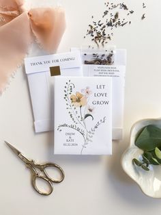 a pair of scissors and some cards on a white table with pink flowers in the background