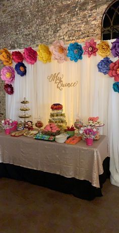 a table topped with lots of desserts under a white drape covered wall next to a window