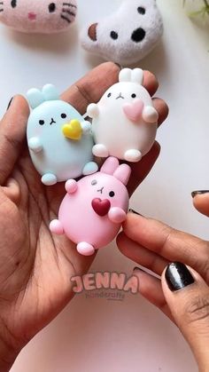 a person holding three small toy animals in their hands, one is pink and the other is blue