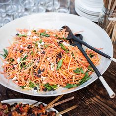 a white plate topped with carrot salad next to other plates and utensils on top of a wooden table