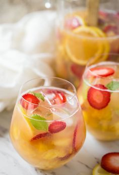 two glasses filled with fruit punch on top of a wooden table next to sliced oranges and kiwi