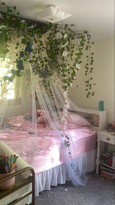 a bedroom with a bed covered in pink sheets and plants hanging from the ceiling above it