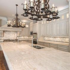 a chandelier hanging from the ceiling in a kitchen with marble counter tops and white cabinets