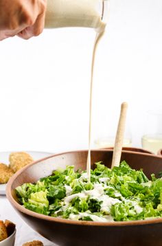 a person pouring dressing into a bowl filled with lettuce and crackers on the side