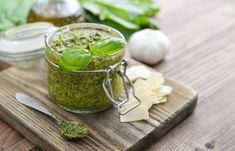 pesto in a glass jar on a cutting board with garlic, basil and parmesan cheese