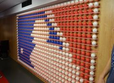 a man standing in front of a wall with baseballs on it and an american flag made out of balls