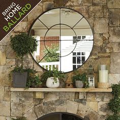 a stone fireplace with potted plants and a round mirror on it's mantle