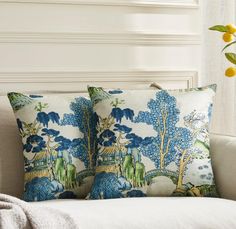 two blue and white pillows sitting on top of a couch next to a plant in a vase