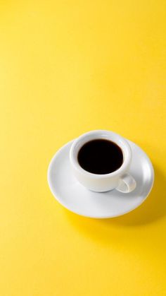 a cup of coffee sitting on top of a white saucer next to a yellow background