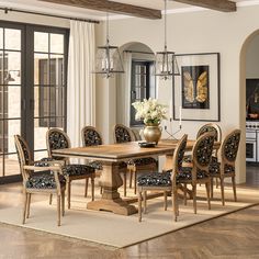 a dining room table surrounded by chairs and chandelier with flowers in vase on top