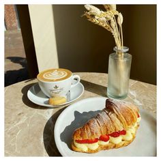 a croissant sandwich on a plate next to a cup of coffee