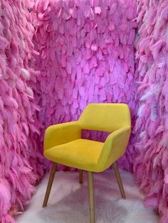 a yellow chair sitting in front of a wall covered with pink and purple feathered walls