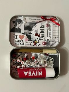 two tins filled with charms and other items on a white surface, next to each other