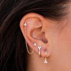 a close up of a woman's ear wearing gold chain and flower shaped earrings