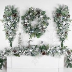 christmas wreaths and pine cones are arranged on top of a fireplace mantel with silver ornaments