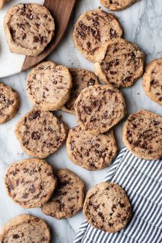 chocolate chip cookies on a marble surface with a wooden spoon and striped towel next to them