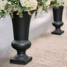 two black vases with white flowers are on the ground next to eachother