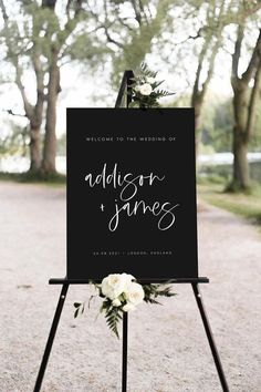 a sign that is on top of a tripod in the dirt with flowers and greenery