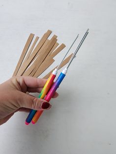 a person holding several different colored toothbrushes in one hand and two wooden sticks sticking out of the other