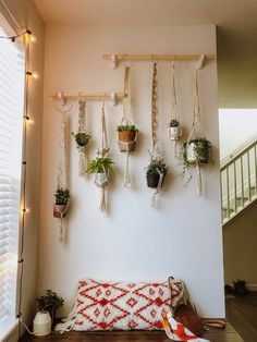 a wall with hanging planters and potted plants on the top of it, next to a wooden bench