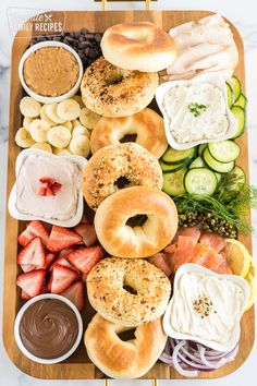 an assortment of bagels and dips on a wooden platter with strawberries