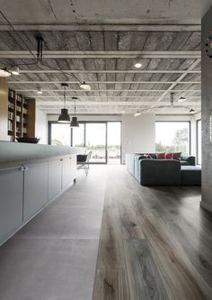 an open living room and kitchen area with wood flooring, exposed ceilings, and large windows