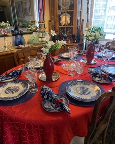 a red table cloth with blue and white plates on it is set for a formal dinner