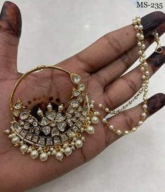 a woman's hand holding a pair of gold and pearl earrings with chains attached to it