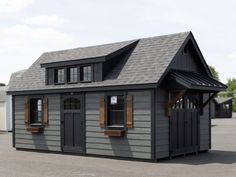 a small gray building with two windows and a porch on the roof is shown in an empty parking lot