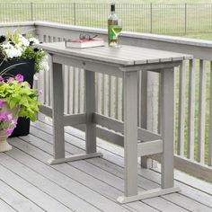 a wooden table sitting on top of a porch next to potted plants and a bottle of wine